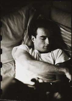 a black and white photo of a man laying in bed with his arms folded out