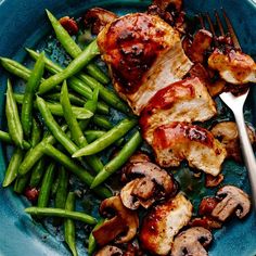 a blue plate topped with meat, green beans and mushrooms next to a silver fork