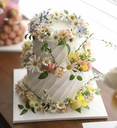 a three tiered cake decorated with flowers and greenery sits on a wooden table