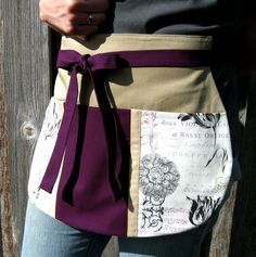 a woman wearing a purple and tan apron with flowers on it's front pocket