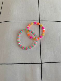 two bracelets sitting on top of a white tile floor next to an orange, yellow and pink beaded bracelet