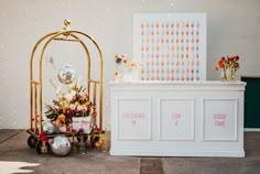 a white and gold wedding reception set up with flowers on the side table, silver vases in front of it