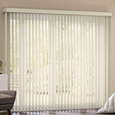 a living room with white vertical blinds in the window and a chair next to it