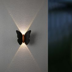 a wall light with a butterfly on it's side next to a white wall