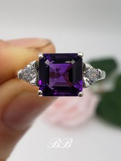 Made to order.  Please allow up to 3 weeks for the production of your ring. This listing is for a 925 non-plated sterling silver or non-plated gold ring with a natural dark purple amethyst asscher cut center stone in the size of your choosing. Photos show the 8mm sterling silver. Amethyst Asscher Cut Center Stone Sizes 7mm (2 Carat Approximately) 8mm (2.5 Carat Approximately) Center Stone Gem Type: Natural Amethyst Shape: Asscher Cut Size: Your Choice Color: Dark Purple Quality: AAA Hardness: 9 Mohs Accent Stones Gem Type: Lab Created Cubic Zirconia Diamonds Shape: Trillion Cut Size: (2) 4mm Color: White Colorless Quality: 6A Hardness: 8.5 Mohs Metal Selection (all metals are solid and non-plated) 925 Sterling Silver 10KT White Gold (non-rhodium plated) 10KT Yellow Gold 14KT White Gold (no Luxury Purple Jewelry With Center Stone, Luxury Purple Jewelry For Anniversary, Luxury Purple Amethyst Ring In Sterling Silver, Luxury Amethyst Ring With Center Stone For Gift, Luxury Amethyst Ring With Center Stone As A Gift, Classic Purple Ring As Gift, Classic Purple Rings As Gift, Classic Purple Jewelry For Promise, Elegant Sterling Silver Solitaire Gemstone