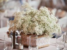 an arrangement of white flowers in a vase on a table with wine glasses and napkins