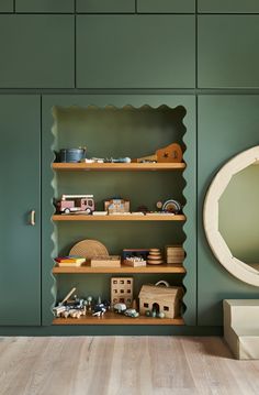 a green room with wooden shelves and toys on the bottom shelf in front of a round mirror