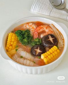 a bowl of soup with shrimp, broccoli and other vegetables on the side