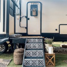 an rv with stairs leading up to the front door and side porch area, next to potted plants