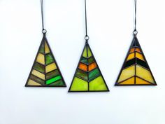 three stained glass ornaments hanging from strings on a white wall in the shape of triangulars