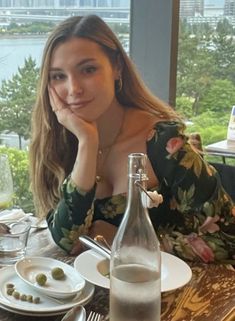 a woman sitting at a table in front of a bottle and plate with food on it