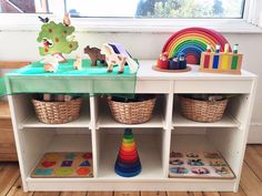 a toy table with toys on it in front of a window and some bookshelves