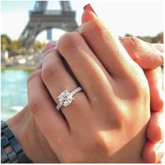 two people holding hands in front of the eiffel tower, with their engagement rings on their fingers