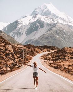 a woman walking down the middle of a road with mountains in the backgroud