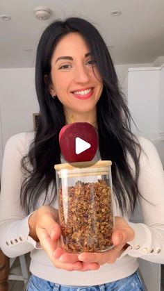 a woman is holding an apple in a jar with granola inside it and smiling