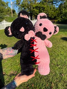 a person holding two black and pink stuffed animals in their hands with tattoos on their arms