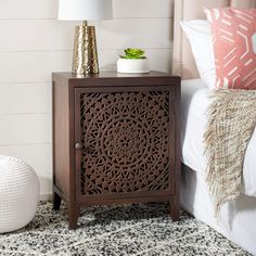 a nightstand with a plant on top of it next to a white rug and pillows