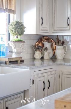 a kitchen with white cabinets and marble counter tops is pictured in this image, there are two vases on the wall above the sink