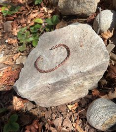 a rock with a ring on it sitting in the dirt next to rocks and leaves