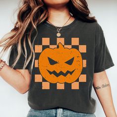 Celebrate the spooky season in style with our adorable jack o' lantern T-shirt! Featuring a classic jack o' lantern design on an orange checkerboard background, this charming shirt adds a fun and festive touch to your Halloween wardrobe. Perfect for Halloween parties, casual outings, or simply showcasing your love for all things Halloween, this tee is a must-have for the season. Made from soft, high-quality fabric, it ensures comfort while you enjoy the festivities. Order your jack o' lantern sh Spooky Orange T-shirt For Fall, Orange Spooky T-shirt For Fall, Spooky Orange Fall T-shirt, Spooky Halloween Tops, Checkerboard Background, Vintage Halloween Pumpkin, Halloween Top, Lantern Design, Halloween Shirts