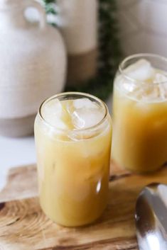 two glasses filled with drinks sitting on top of a wooden cutting board