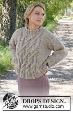 a woman standing in front of trees wearing a sweater