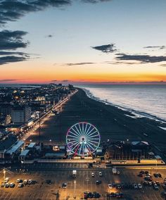 an aerial view of a ferris wheel and the ocean at dusk with cars parked on the road