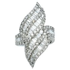 Ring size: 7.5 This lustrous, sparkling cocktail ring is a captivating embodiment of modern artistry and timeless luxury. Crafted in shimmering 14 karat white gold, its design is a marvel, resembling fiery flames that dance with movement. This distinctive ornament is adorned with a mesmerizing array of baguette and round diamonds, which, in unison, create an intricate play of light and shadow. The elegant piece absolutely glows, drawing all eyes to the hand and flattering the finger with its elongated silhouette. The diamonds, both round and baguette-cut, continue their scintillating journey along the shank of the ring, ensuring that elegant shimmer and sparkle grace every facet of this opulent creation. The high polish of the white gold adds more reflective glimmer to this piece, further Sparkling Cocktail, Timeless Luxury, Fine Jewelry Collection, Baguette Cut, Brilliant Diamond, All About Eyes, Ring Size 7, Cocktail Ring, Diamond Clarity