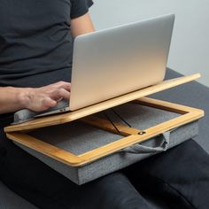 a person sitting on a couch using a laptop computer with a wooden tray attached to it