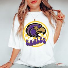 Get this popular new Eagles Mascot shirt and show off your school spirit in style!  Each shirt is printed in-house by me using high-quality materials on a Comfort Colors shirt, known for its exceptional comfort, style, and durability. Even the glitter is printed! No need to worry about peeling glitter vinyl, or messy glitter flakes. Available in unisex sizes S to 3X, and youth sizes, we've got you covered regardless of your preferred fit. The Preppy Eagles Shirt features a classic crew neck and short sleeves, making it suitable for year-round wear. The flattering silhouette ensures a comfortable and stylish fit for both men and women. Please note that ivory is ONLY available in Adult sizes!  Note: As each shirt is individually printed, slight variations in color and placement may occur, ad Team Spirit Graphic Print School T-shirt, Team Spirit Graphic T-shirt For School, Sports Fan Shirt With Graphic Print For Fan Gear, School Team Spirit Graphic T-shirt, Cotton Shirt With Sublimation Print For Fan Gear, Team-colored Fan Apparel Shirt With Graphic Print, Team-colored Shirt With Graphic Print For Fans, Team-colored Graphic Print T-shirt For School, Team-colored Graphic Print Shirt For Fans