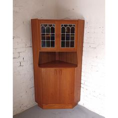 a wooden cabinet with stained glass doors on the top and bottom shelf, against a white brick wall