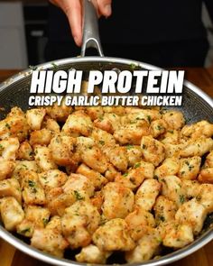 a pan filled with chicken sitting on top of a wooden table next to a person holding a spoon