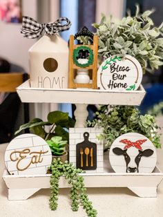 two tiered trays holding decorative items on top of a table with greenery