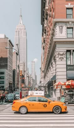 a yellow taxi cab driving down a street next to tall buildings in new york city