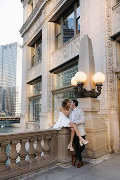 a man and woman are sitting on a ledge in front of a building with lights