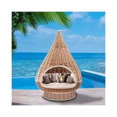 a wicker hanging chair with pillows on the deck next to an outdoor pool and ocean view