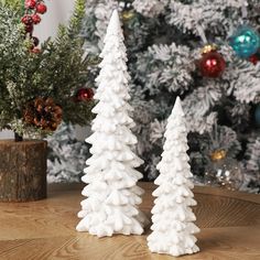 two white christmas trees sitting on top of a wooden table