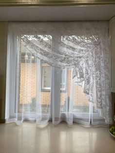 an open window with curtains and fruit on the counter