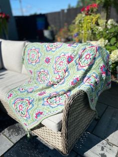 a couch with a blanket on top of it sitting in front of some flowers and bushes