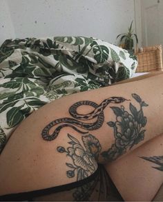 a woman laying on top of a bed with a snake tattoo on her thigh and leg