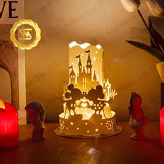 a lighted cake with mickey and minnie mouse figurines next to it on a table