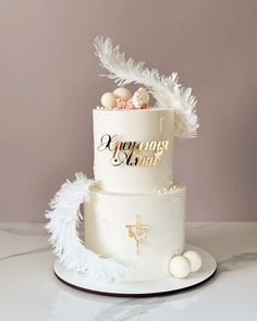 a three tiered cake with white feathers on top and gold lettering in the middle