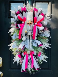 a christmas wreath on the front door of a house decorated with pink, white and grey ribbons