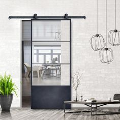 an open glass door leading to a living room with white walls and wooden floors, surrounded by potted plants