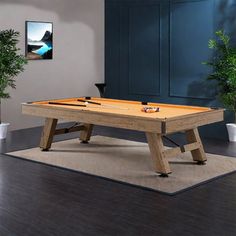 a pool table sitting on top of a hard wood floor next to potted plants