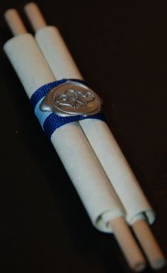 three white napkins with blue ribbon around them on a black table top, one has a button and the other has a silver metal clasp