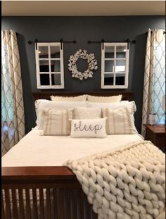 a bed with pillows and blankets on top of it in front of two framed windows