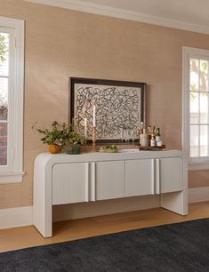 a white console table with candles on it in front of two windows and a rug