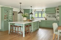 a kitchen with green cabinets and white counter tops, wooden floors and stools in front of the island