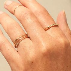 A hand with light freckles and bare nails wears stacks of gold rings. On the ring finer are three painter's rings that are thin bands of solid gold with natural curves like liquid metal. On the pointer finger is the bigger sister of those painter's rings. It is a thicker version of the classic painter's ring. Modern Twisted Rings As A Gift, Minimalist Twisted Yellow Gold Ring, Modern Twist Yellow Gold Bypass Ring, Gold Bypass Ring With Modern Twist, Adjustable Twisted Wedding Rings, Minimalist Twisted Gold Rings, Gold Rings With A Modern Twist, Twisted 14k Gold Rings With Modern Twist, Modern Gold Ring With Polished Finish